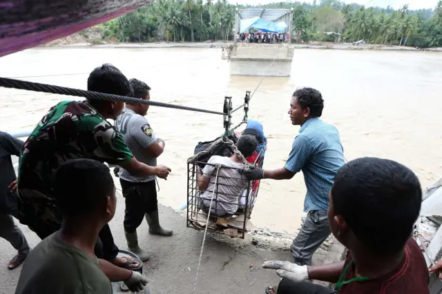 Warga menggunakan kabel baja yang untuk menyeberangi Sungai Juli pascaputusnya Jembatan Juli di jalan lintas Bireuen - Takengon, Aceh, Selasa (2/12/2025). 