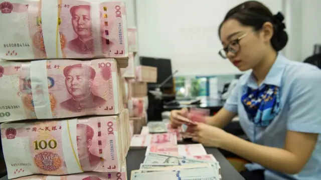 A Chinese bank employee counts 100-yuan notes and US dollar bills at a bank counter in Nantong in China's eastern Jiangsu province on August 28, 2019.