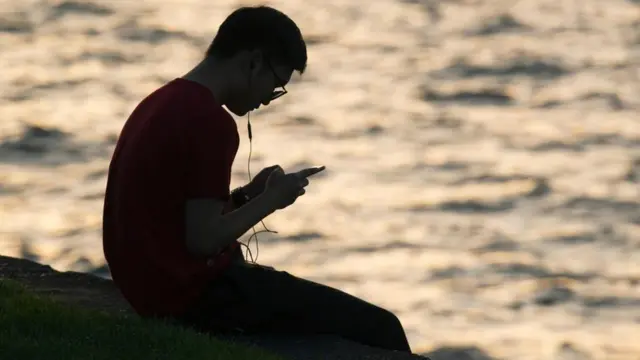 Homem usa celular na beira d'água