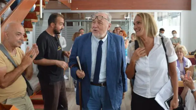 ilber ortaylı gözlüklerini kafasına takmış, yanında bir başka kadın hoca var etrafında onları alkışlayanlara bakıyorlar.