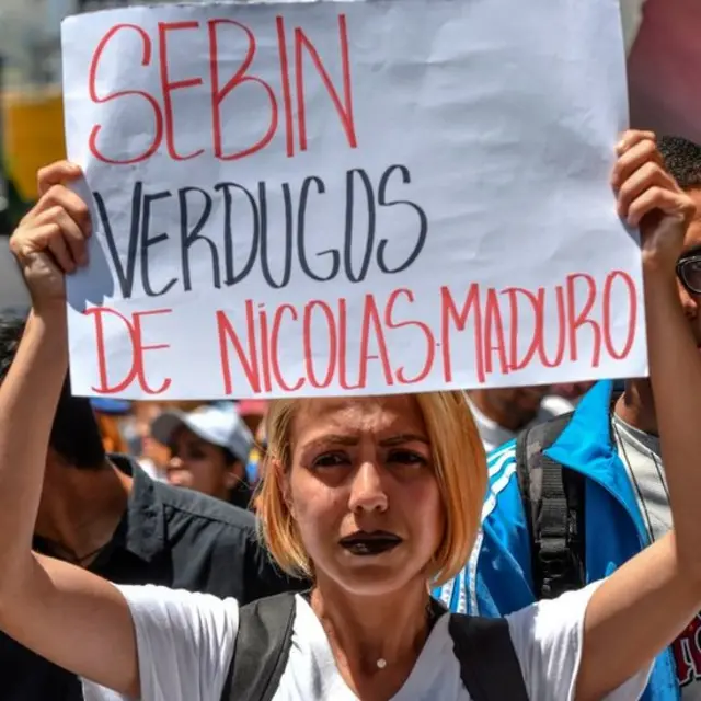 Mulher ergue cartaz com os dizeres 'Sebin: Carrascosroleta do bichoNicolás Maduro'