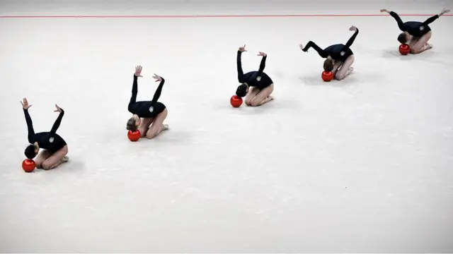 Five gymnasts perform gymnastic movements with red balls