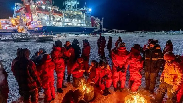 Researchers gathered around camp fire. Polarstern is seen in the background.