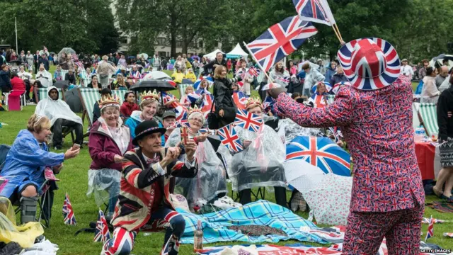 Joseph Afrane, 52, in Union Jack clothing waves flags as members of the public in Green Park gather for a picnic and watch The Queen"s Patronage on a big screen during "The Patron's Lunch" celebrations