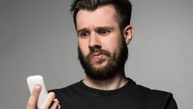 joven mirando con extrañeza un celular