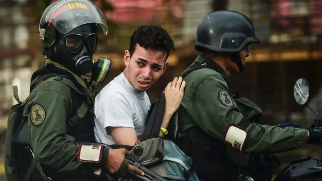 Dos funcionaros de la Guardia Nacional Bolivariana se llevan a un joven detenido.