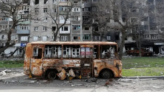 Imodoka ya bisi yahiye iboneka imbere y'inyubako yo guturamo yangijwe mu ntambara ya Ukraine n'Uburusiya, mu mujyi wo ku cyambu mu majyepfo wa Mariupol, muri Ukraine, ku itariki ya 19 y'ukwezi kwa kane mu 2022