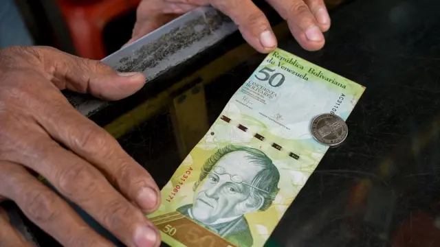 Un hombre compara un billete con una moneda venezolana del mismo valor.