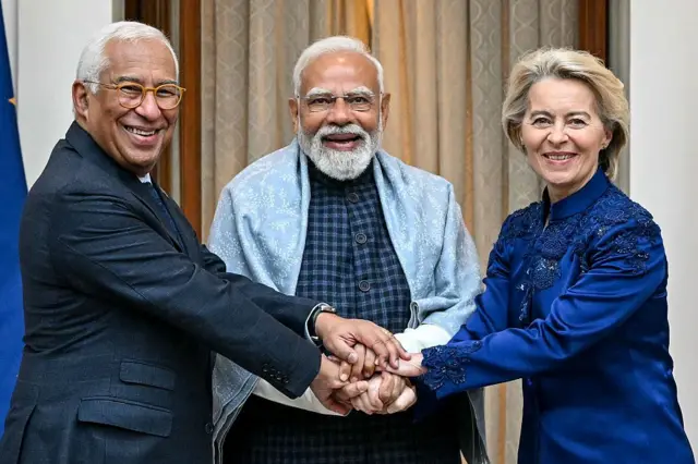 De izquierda a derecha, el presidente del Consejo Europeo, Antonio Costa; el primer ministro indio, Narendra Modi; y la presidenta de la Comisión Europea, Ursula von der Leyen. Sonríen a la cámara y tienen sus manos entrelazadas.
