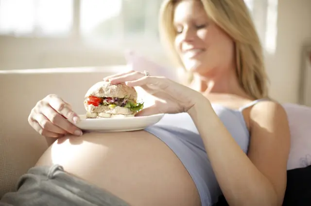 Mulher grávida comendo hamburguer