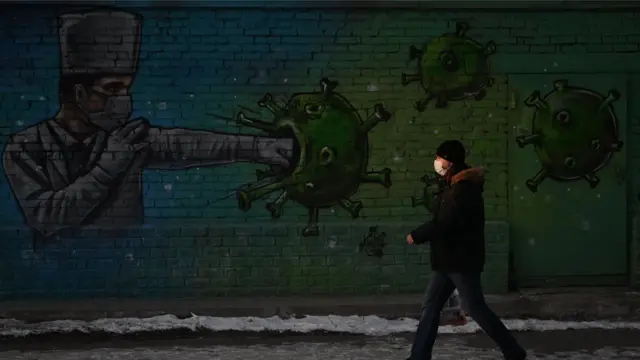 A man wearing a protective face mask walks past a graffiti depicting a healthcare worker fighting the virus, amid the outbreak of the coronavirus disease (COVID-19) in Omsk, Russia November 23, 2020