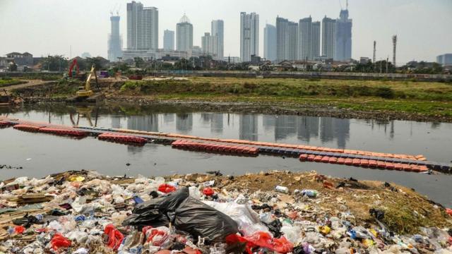 Plastic waste on the banks of a river with a view of the Jakarta skyline (file photo - August 2019)