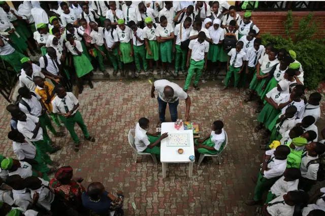 Fazil Omar Senior high school students play the "enter ball" game as the game developer Oluwaseun Sanni directs a game session during a time-out in Lagos' Iwaya community. The game is played with dice and two cowrie shells on a board.