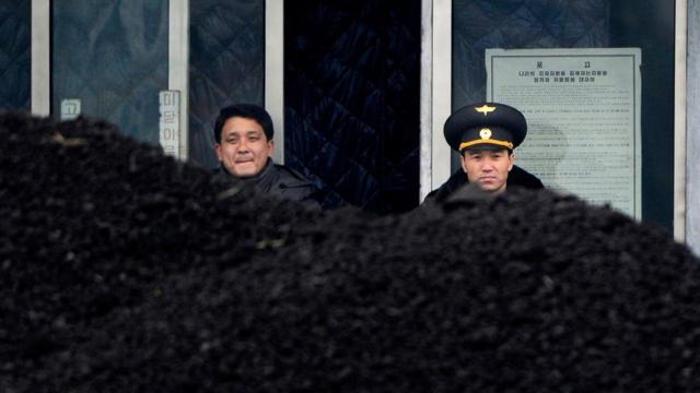 2012年12月、北朝鮮・新義州で積まれた石炭を前に立つ北朝鮮将校と北朝鮮男性を、国境を挟んだ中国・丹東から撮影。