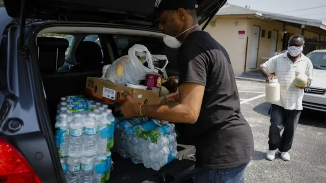 Un hombre llena su maletero de agua y alimentos