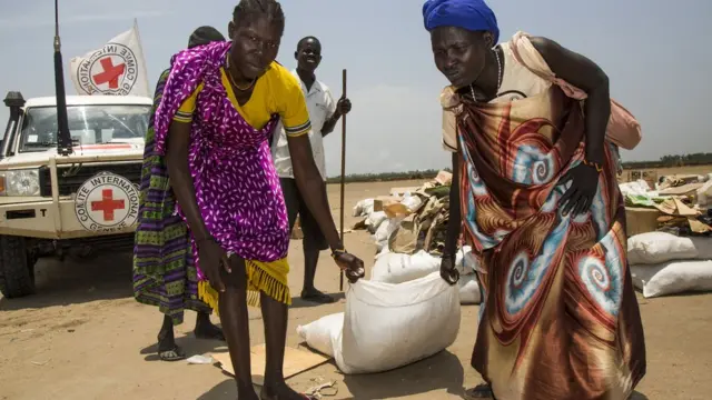 Awọn obinrin meji n gbe apo ounjẹ kan niwaju ọkọ ẹgbẹ alagbelebu pupa