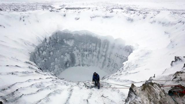 Buraco enorme no gelo, com uma pessoa fazendo rapel para descer