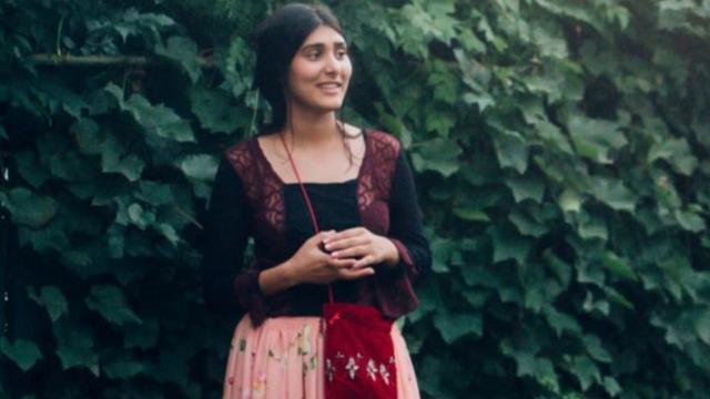 Izabela Tiberiade vestindo vestido tradicionaljogos de cozinharfrente a parede com plantas