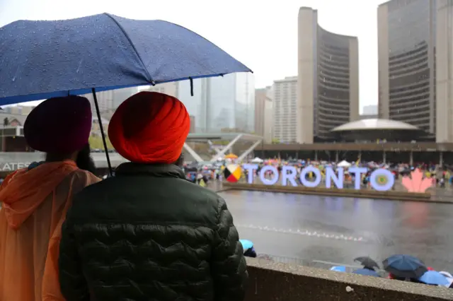 People standing on a rainy day outside gather to commemorate 'Sikh New Year' in Toronto (April 2023) ටොරොන්ටෝ හි 'සීක් අලුත් අවුරුද්ද' සැමරීමට මිනිසුන් රැස් වෙති (අප්‍රේල් 2023) 