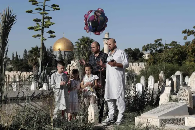 Palestinians pray over the grave of a loved one at a Muslim cemetery near the Al-Aqsa Mosque compound in Jerusalem's Old City, 25 June
