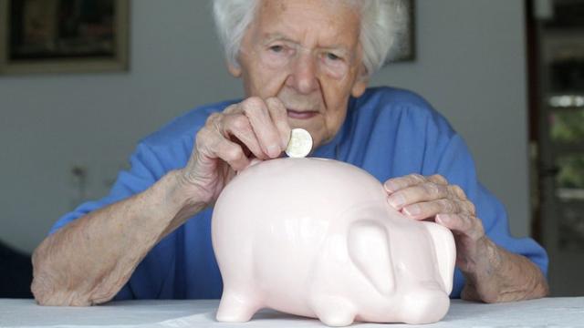 Mujer adulta deposita una moneda en una alcancía con forma de cerdo rosa.