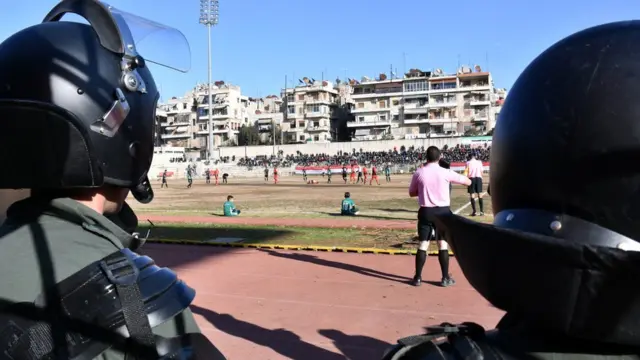 The helmets of two Syrian police, in full riot gear, are seen watching the football game from the sidelines