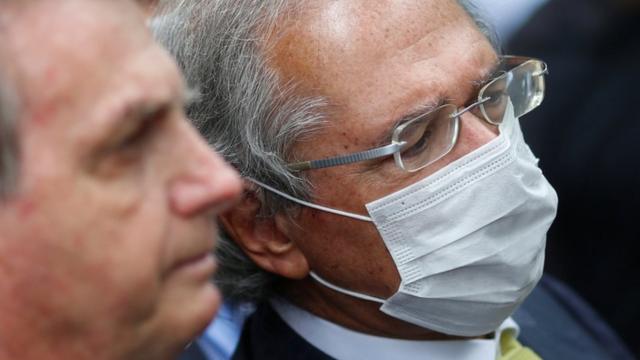 O presidente Jair Bolsonaro e o ministro Paulo Guedes, de máscara, aparecem de perfil