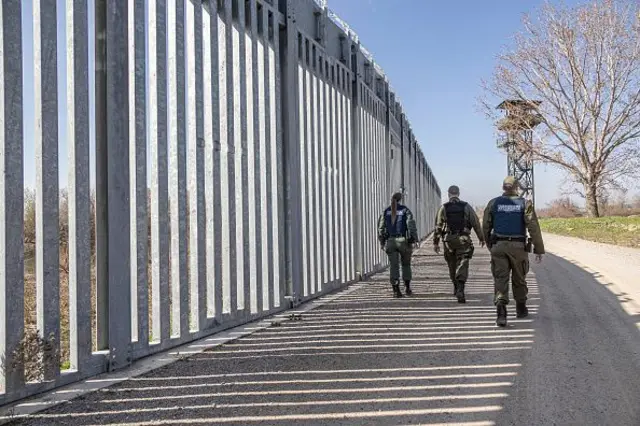 Yunanistan sınırında devriye gezen üç polis duvarın yanında arkadan görünüyor. Nisan 2023. 