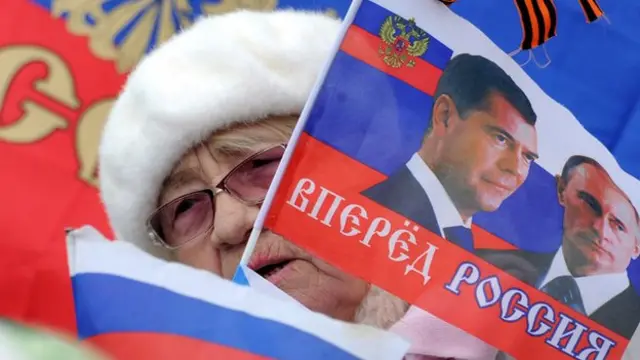 A woman holds a flag depicting Russian President Vladimir Putin and Russian Prime Minister Dmitriy Medvedev during a rally in Sevastopol on 17 March 2014.