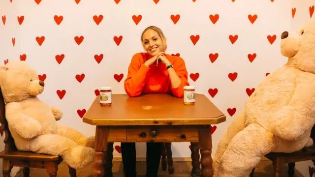 devojka sedi za stolom između dve plišane igračke