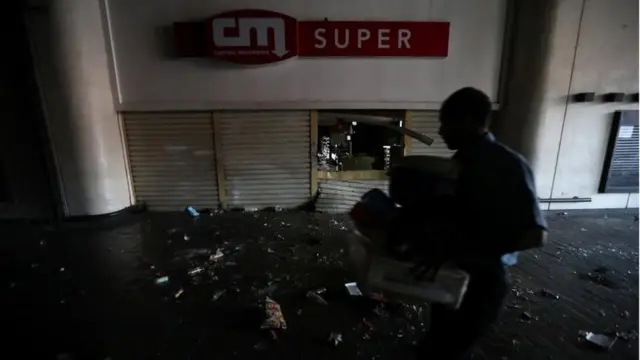 A shop employee helps clean up the area after the shop was looted during an ongoing blackout in Caracas, Venezuela, March 10, 2019.