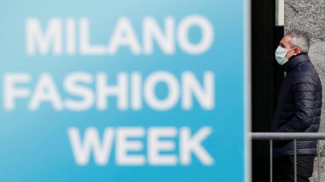 человек в маске на фоне стенда Миланской недели моды