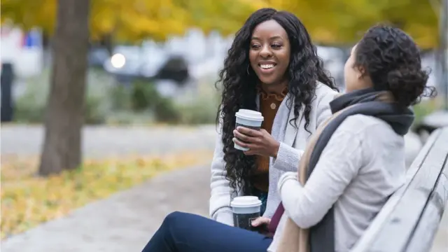 Duas mulheres sentadas num banco ao ar livre tomando café