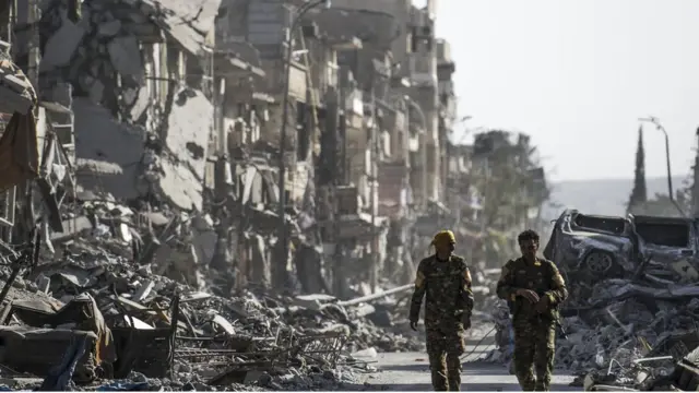 కూలి పోయిన భవనాల మధ్య నడుస్తున్న సైనికులు