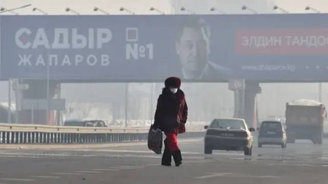 Женщина на фоне предвыборного плаката Жапарова в густом смоге
