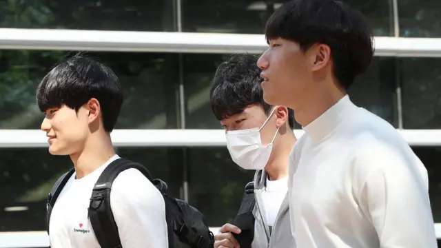 마스크를 쓴 학생 1명과 마스크를 벗은 학생 2명이 함께 캠퍼스를 걷고 있다