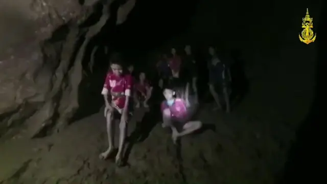 Tham Luang cave, Thailand. Boys trapped in a cave are seen sitting on a dry piece of land in a dark cave lit by a torch