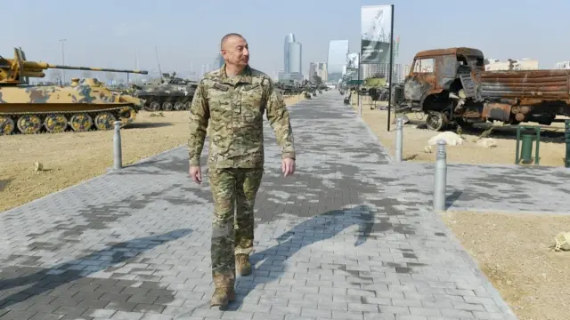Алиев на фоне танков и военных машин.