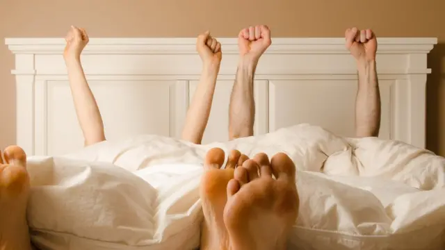 Pareja en la cama con actitud victoriosa.