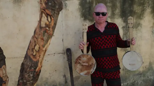 Lazare brandit deux instruments à cordes improvisés