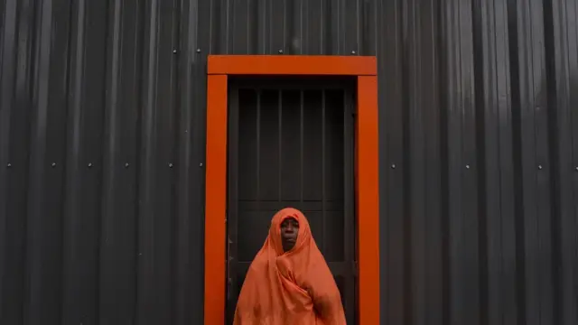 Woman in red outfit standing behind a black wall. There is a red doorframe that matches her outfit