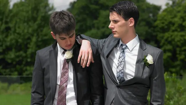 Dos hermanos con traje expresando una mirada de rivalidad.