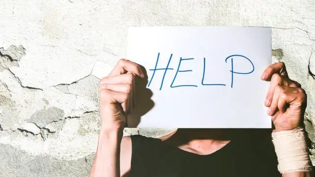 Mujer con un cartel tapándole la cara con la palabra ayuda.
