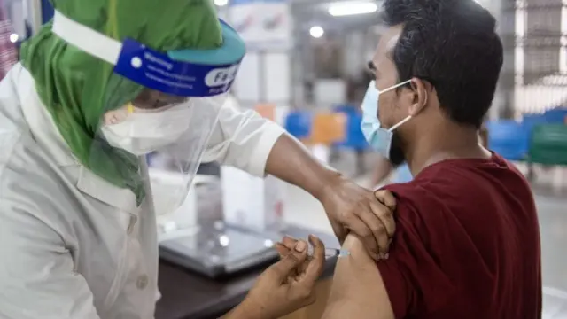 Un homme est vacciné par une femme avec un masque de protection au Bangladesh.