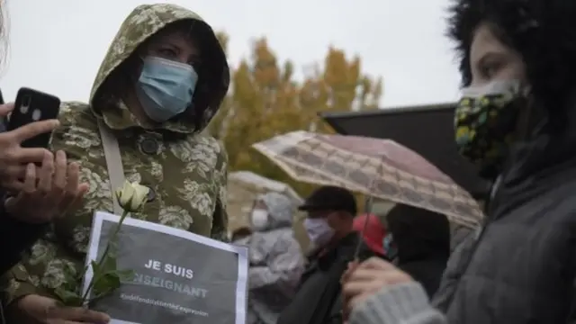 Mengenang guru sejarah yang dipenggal, warga memegang tulisan, "Saya guru."