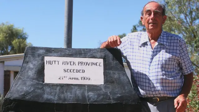 Leonard Casley frente a una placa que conmemora el día en el que declaró su estado independiente el 21 de abril de 1970.