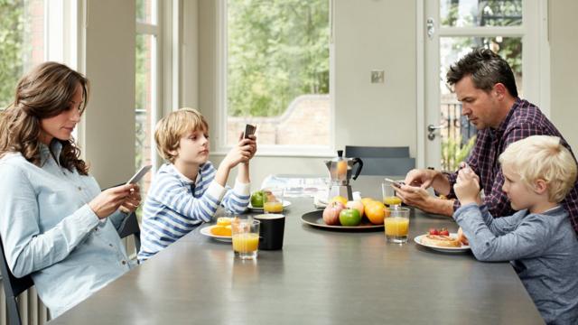 Família olhando o celular enquanto come