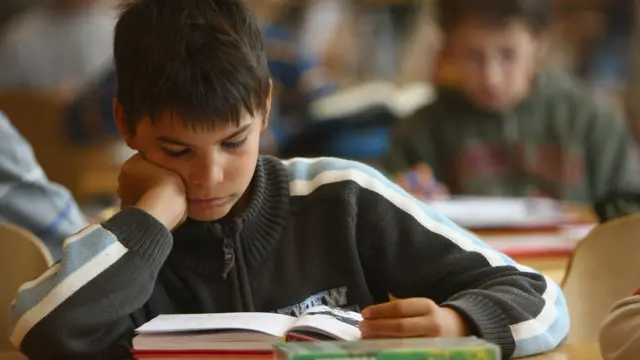Niño lee un libro en una clase.