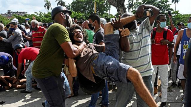 Manifestante sendo carregado durante protesto em Cuba neste domingo