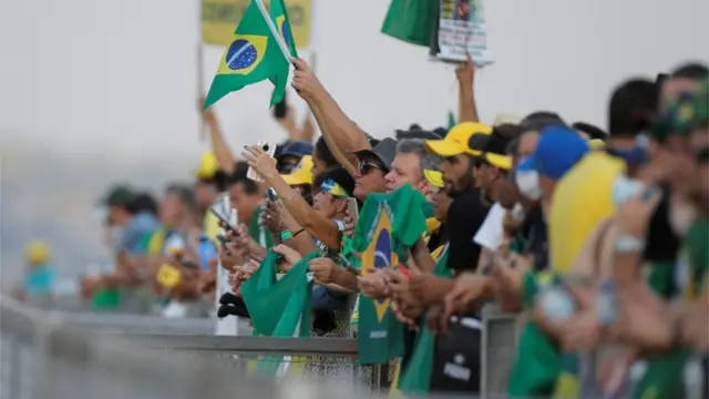 Pessoas com roupas verde, amarelo e azul atrás de cerca